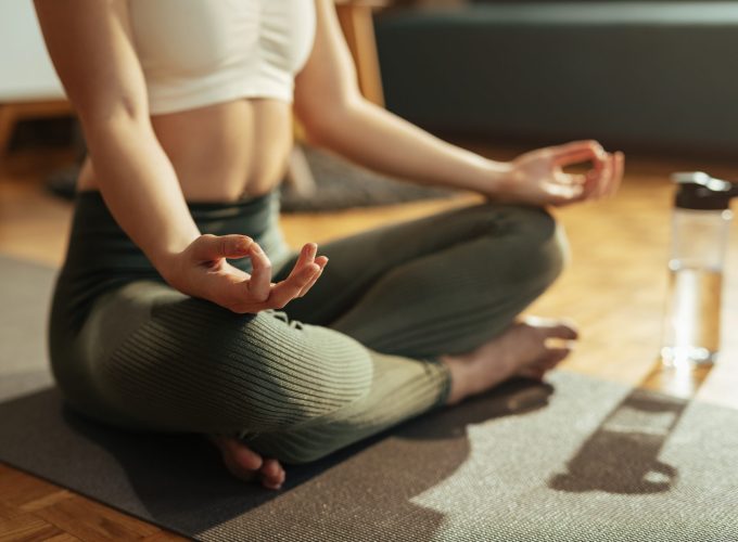 Close-up of woman meditating on lotus position at home.